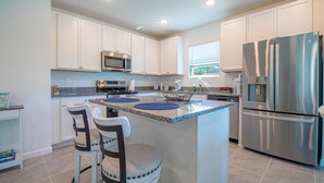 A modern kitchen with white cabinets, a stainless steel refrigerator, a microwave, and a granite countertop. - Escape the Winter! Cozy 3BR Retreat in Sunny Ocala, Florida (Ocala)