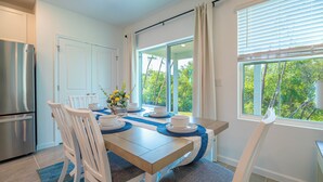 A modern kitchen with a stainless steel refrigerator, white cabinetry, and a dining area with a wooden table, white chairs, and a view of greenery through large windows. - Escape the Winter! Cozy 3BR Retreat in Sunny Ocala, Florida (Ocala)