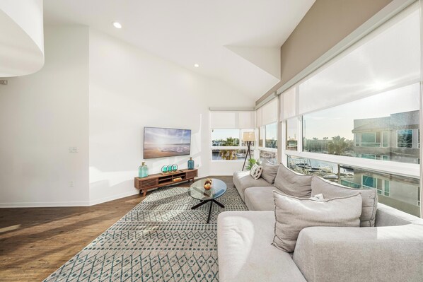 A modern living room with a large window, a sofa, a coffee table, and a TV. - The Navagio' Waterfront Penthouse 3 Levels, Private Rooftop Boats View Parking (Marina del Rey)