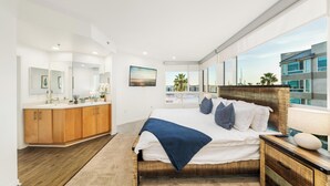A modern bedroom with a large bed, wooden headboard, and a view of a building through large windows. - The Navagio' Waterfront Penthouse 3 Levels, Private Rooftop Boats View Parking (Marina del Rey)