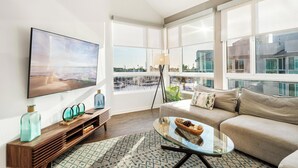 A modern living room with a large flat-screen TV, a sofa, a glass coffee table, and a wooden console table with decorative items. - The Navagio' Waterfront Penthouse 3 Levels, Private Rooftop Boats View Parking (Marina del Rey)