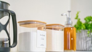 Tres frascos de vidrio con tapas de madera en un estante, uno etiquetado con "SUGAR" y otro con una etiqueta parcialmente visible.