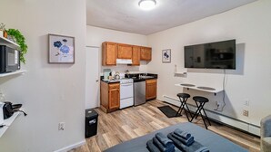 Cocina compacta con armarios de madera, estufa y lavamanos. Zona de comedor con mesa y sillas.