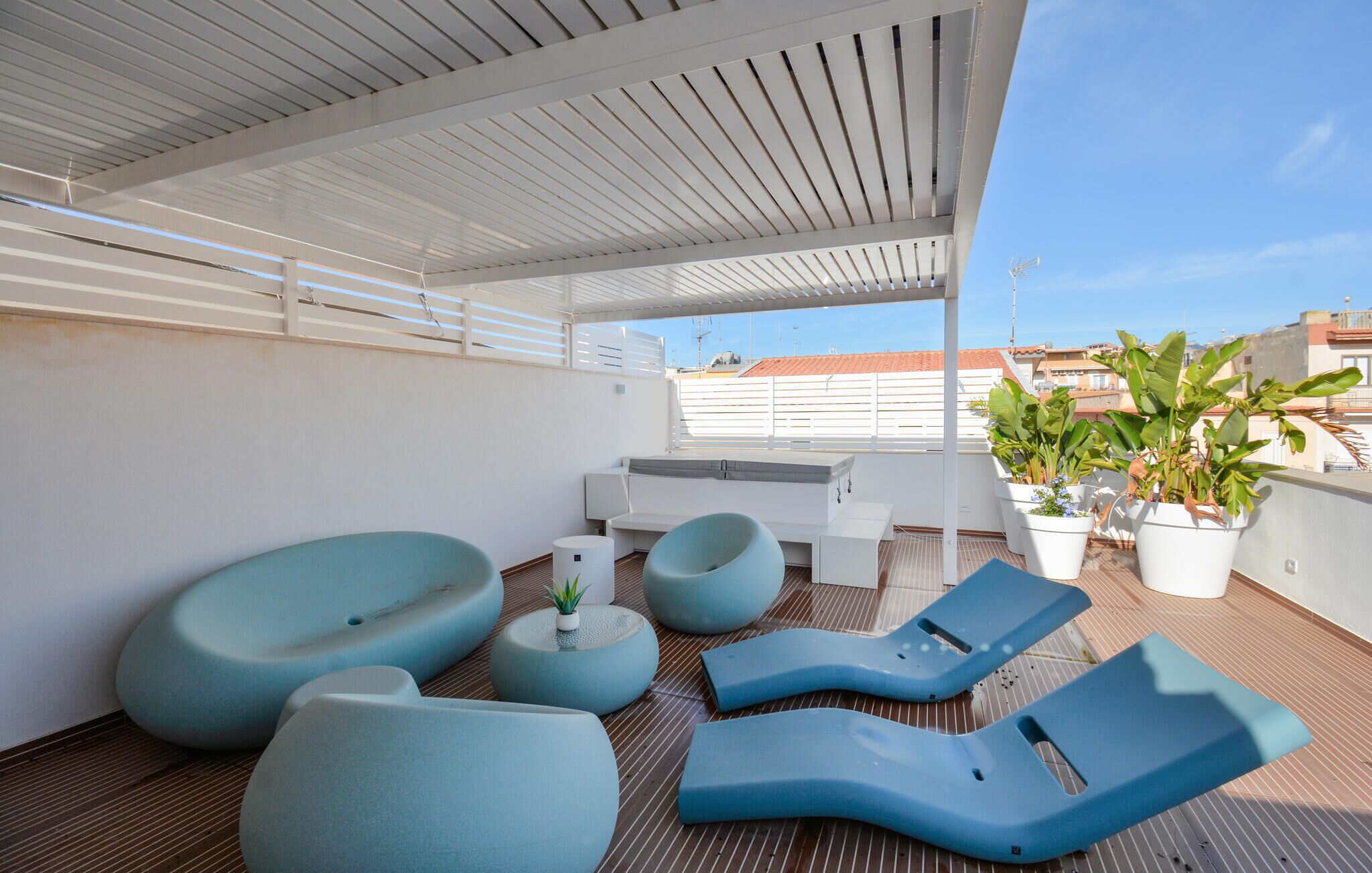 A rooftop terrace with modern seating, a small table, and potted plants.
