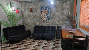 Habitació amb paret de pedra, taula de dinar de fusta amb cadires, un sofà negre i una decoració de paret amb dibuixos.