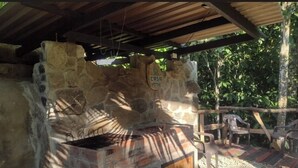 Barbacoa de pedra a l'aire lliure amb una cadira de fusta i zona coberta.
