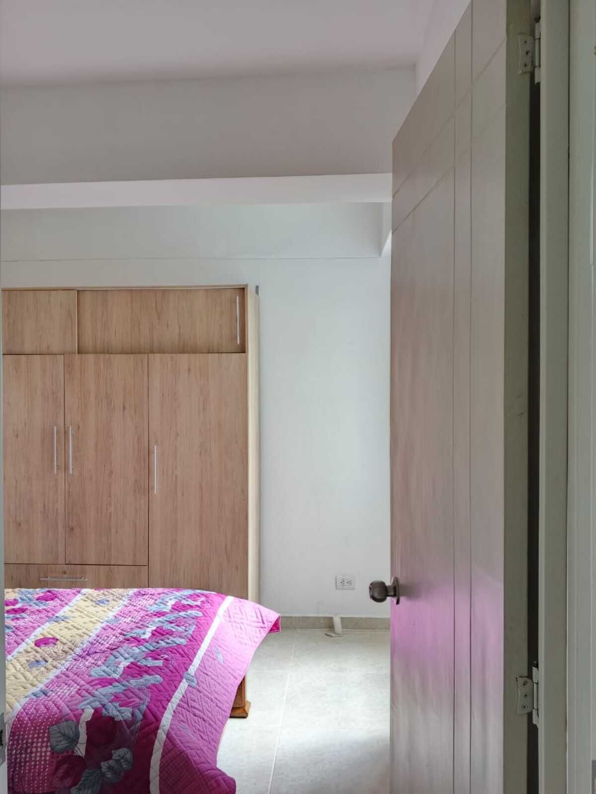 Un dormitorio con un armario de madera, una cama con un colcha de colores y una puerta blanca.