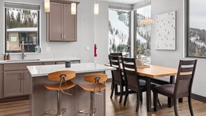 A modern kitchen with a large island, wooden chairs, and pendant lighting. - Modern Mountainside Retreat | Hot Tub & Views (Sandpoint)