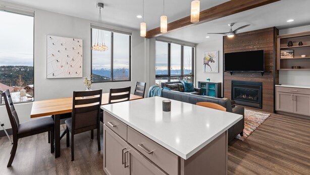 A modern kitchen with a central island, dining area with chairs, a sofa, and a fireplace. - Modern Mountainside Retreat | Hot Tub & Views (Sandpoint)