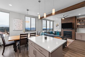 A modern kitchen with a central island, dining area with chairs, a sofa, and a fireplace. - Modern Mountainside Retreat | Hot Tub & Views (Sandpoint)