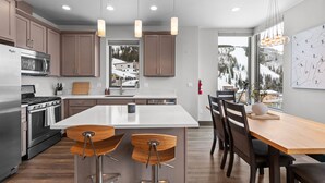 A modern kitchen with a central island, stainless steel appliances, and a view of a snowy landscape. - Modern Mountainside Retreat | Hot Tub & Views (Sandpoint)