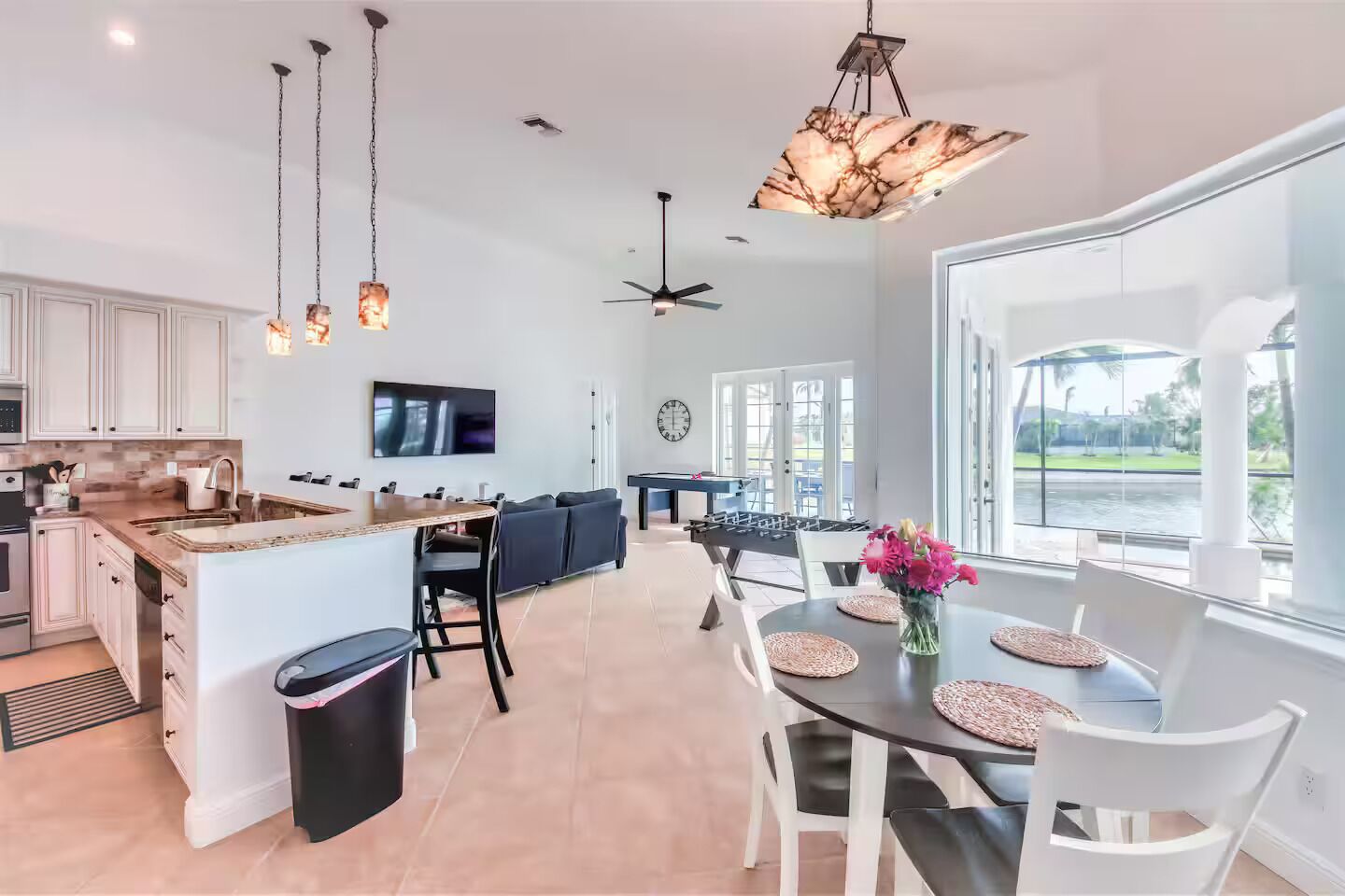 A spacious kitchen with a central island, a dining area with a round table, and a view of a water body through large windows.