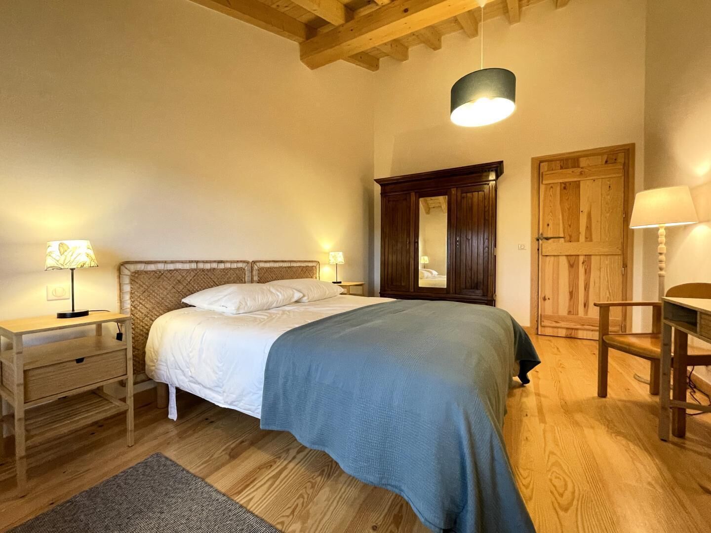 Um quarto com cama, mesas de cabeceira, guarda-roupa e escrivaninha.
