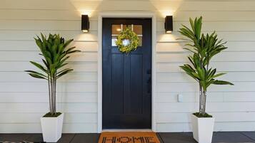 A black door with a wreath, flanked by two potted plants, and a doormat with "HOME" written on it.