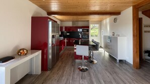 Een moderne keuken met houten balken in het plafond, rode en witte kasten, roestvrijstalen apparatuur en een centraal eiland met barkrukken.