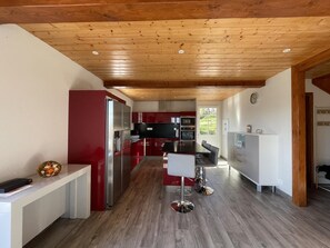 A modern kitchen with wooden ceiling beams, red and white cabinetry, stainless steel appliances, and a central island with bar stools. - MOXOREN BORDA - SARE (SARE)