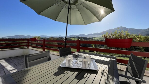 Een houten terras met een tafel gedekt voor twee personen, een rode balustrade en een uitzicht op verre bergen.