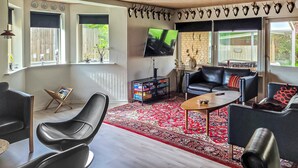 Ein modernes Wohnzimmer mit einem schwarzen Ledersofa, einem roten Teppich mit Muster, einem Fernseher und einem Bücherregal.