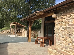 Ein Steingebäude mit einer Pergola, einer Steinsitzbank und einem Grillbereich.