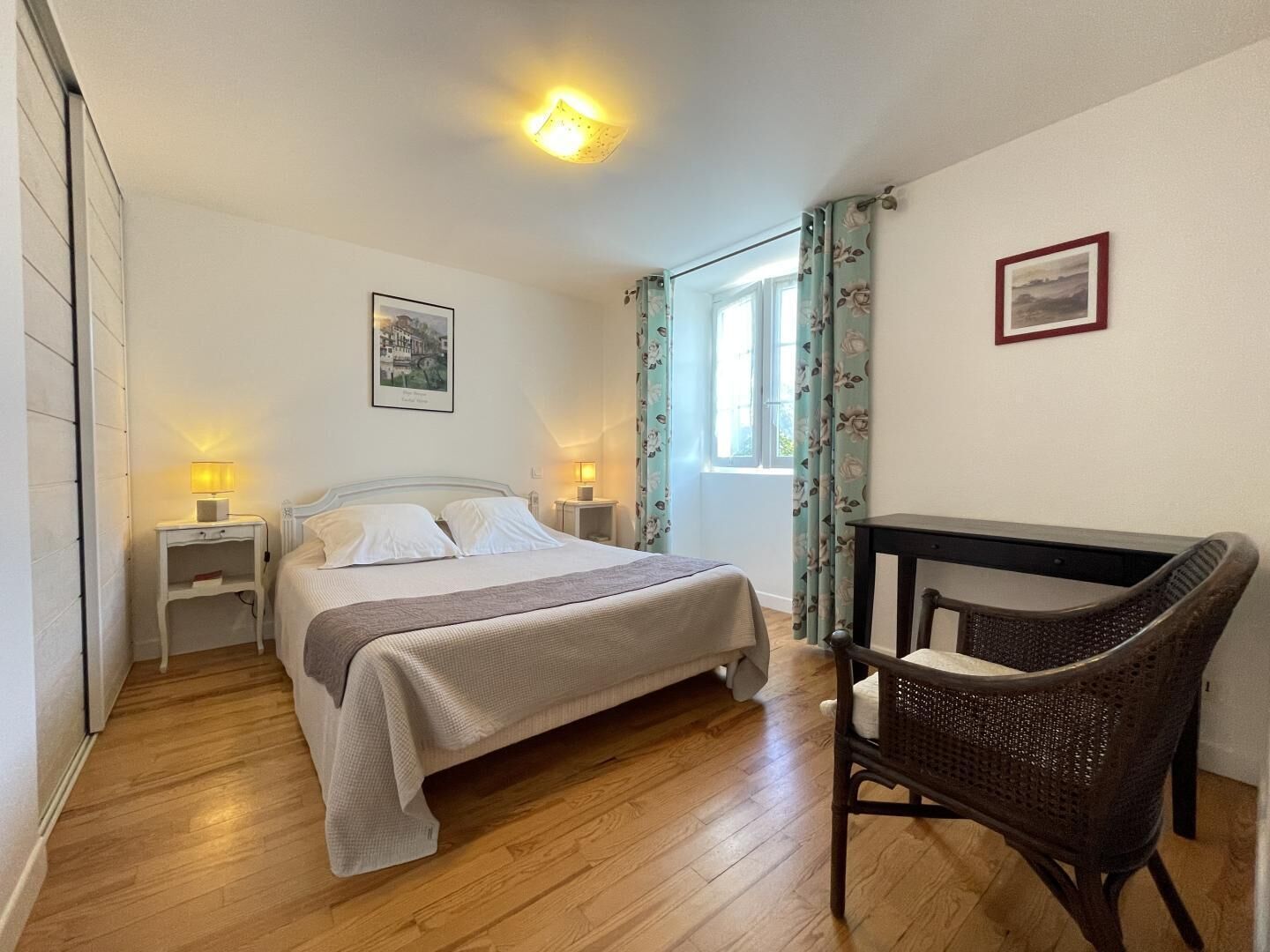 A bedroom with a bed, bedside tables, a chair, a window, and a picture on the wall.