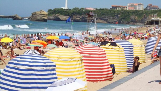 A crowded beach with striped beach umbrellas and a lifeguard tower. - URTXOAK BIXTAN - UHART-CIZE (UHART-CIZE)