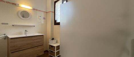 A bathroom with a wooden vanity, a round mirror, and a small window.