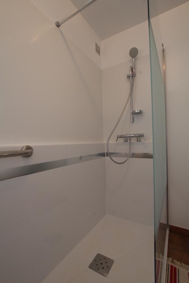 Ducha con mampara de vidrio, cabezal de ducha manual y grifo empotrado.