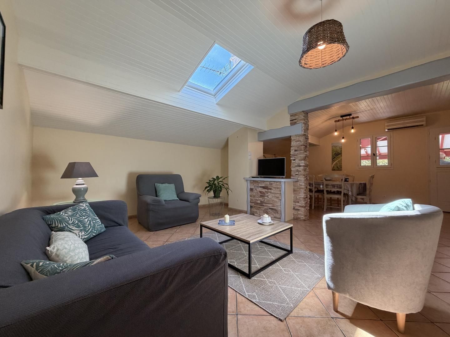 A spacious living area with a high ceiling, a skylight, a flat-screen TV, a dining area, and a cozy seating arrangement.