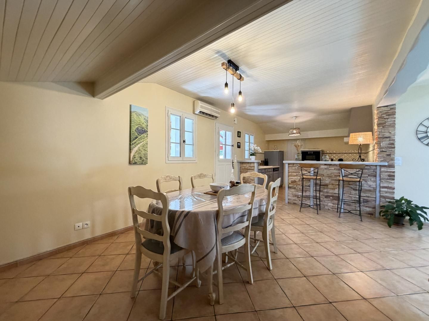 A dining area with a round table and chairs, a kitchen with a stone backsplash, and a clock on the wall.