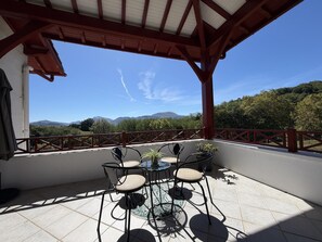 A covered outdoor seating area with a table and chairs, a view of mountains, and a red railing. - BIXTA EDER - MACAYE - B&B (MACAYE)
