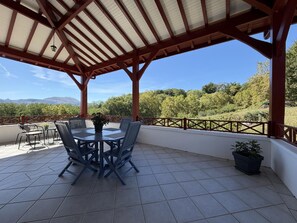 A covered outdoor seating area with a table and chairs, surrounded by a railing, overlooking a forested landscape. - BIXTA EDER - MACAYE - B&B (MACAYE)
