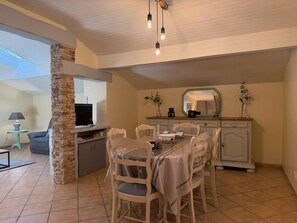 A dining area with a table set for four, surrounded by chairs, a stone pillar, and a television on a stand. - BIXTA EDER - MACAYE - B&B (MACAYE)