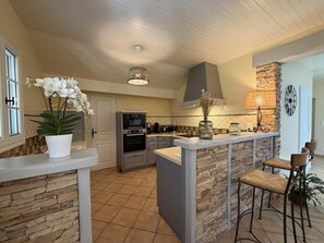 A modern kitchen with a stone accent wall, a built-in oven, and a bar area with stools. - BIXTA EDER - MACAYE - B&B (MACAYE)