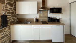 Una cocina compacta con armarios blancos, un lavamanos de acero inoxidable, un microondas integrado y un lavavajillas.