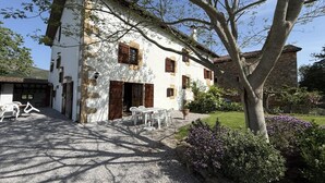 Un edificio blanco con contraventanas marrones, camino de grava y mobiliario exterior.