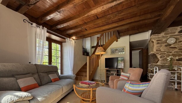 Un salón acogedor con techo de madera, pared de piedra y una escalera.