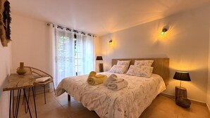 Un dormitorio con una cama, dos lámparas de noche, una mesa con una silla y un ventanal con cortinas.