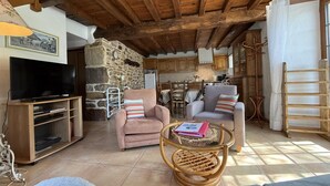 Un salón acogedor con pared de piedra, vigas de madera en el techo, un televisor y dos sofás.