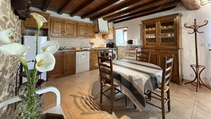 Una cocina rústica con armarios de madera, una mesa de comedor con sillas, un jarrón con flores y un perchero.
