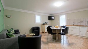 A compact living space with a dining area, a sofa, a TV, and a kitchen with tiled backsplash. - PIERRE BAITA - GUETHARY (GUETHARY)