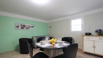 Un coin repas avec une table ronde, des chaises noires, un mur vert, un tableau, une fenêtre et un meuble contenant une radio.