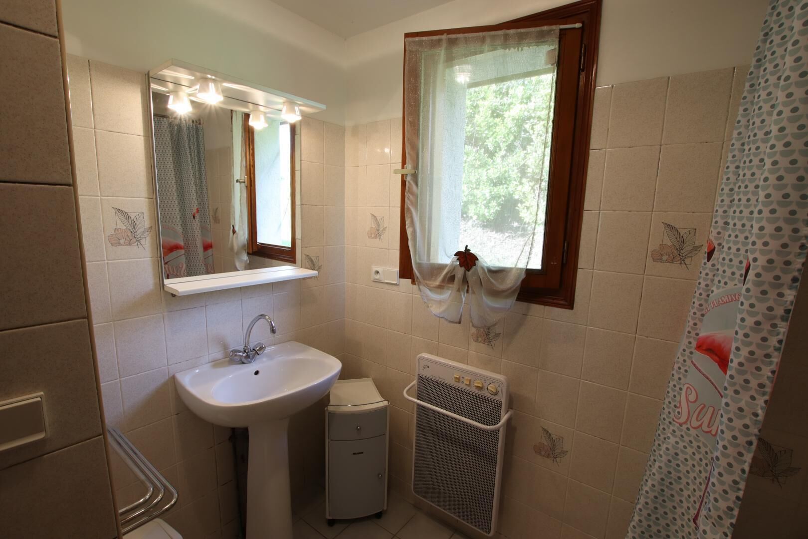 Une salle de bain avec un lavabo, un miroir, une fenêtre et un rideau de douche.