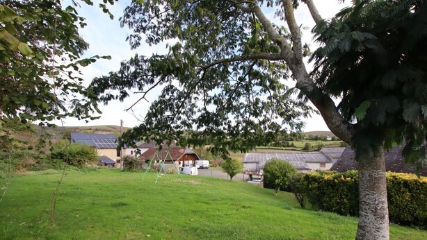 A grassy area with a swing set, a tree, and a building with solar panels in the background. - SALATUA - MUSCULDY - Gîte (MUSCULDY)