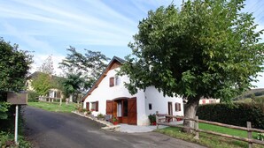 A white house with a wooden door and windows, surrounded by greenery and a fence. - SALATUA - MUSCULDY - Gîte (MUSCULDY)