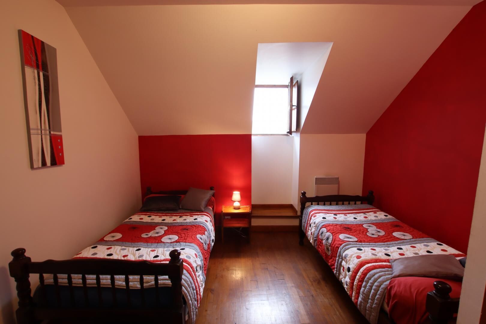 A dormitory room with two beds, a window, a radiator, and a painting on the wall.