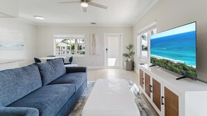 Een moderne woonkamer met een grote flatscreen-tv, een plafondventilator en uitzicht op de oceaan door een groot raam.