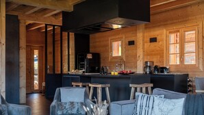 A cozy cabin interior with a wooden interior, a sofa, chairs, a coffee table, and a kitchen area with a stove and sink.