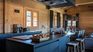 A modern kitchen with wooden walls, a central island with seating, and a dining area with a sofa and bar stools.