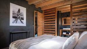 A bedroom with a bed, a wooden slatted wardrobe, a framed picture on the wall, and a small table.