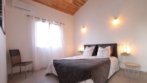 A bedroom with a bed, two bedside lamps, a chair, a small table, and a window with curtains. - JOANESENEA BI - SOURAIDE (SOURAIDE)